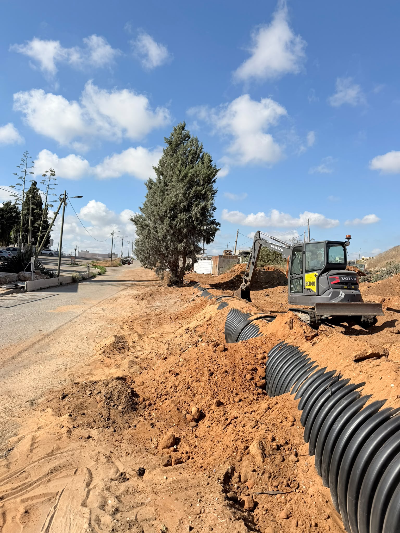 מחפרון מטמין צינור שרשורי שחור גדול באתר בנייה