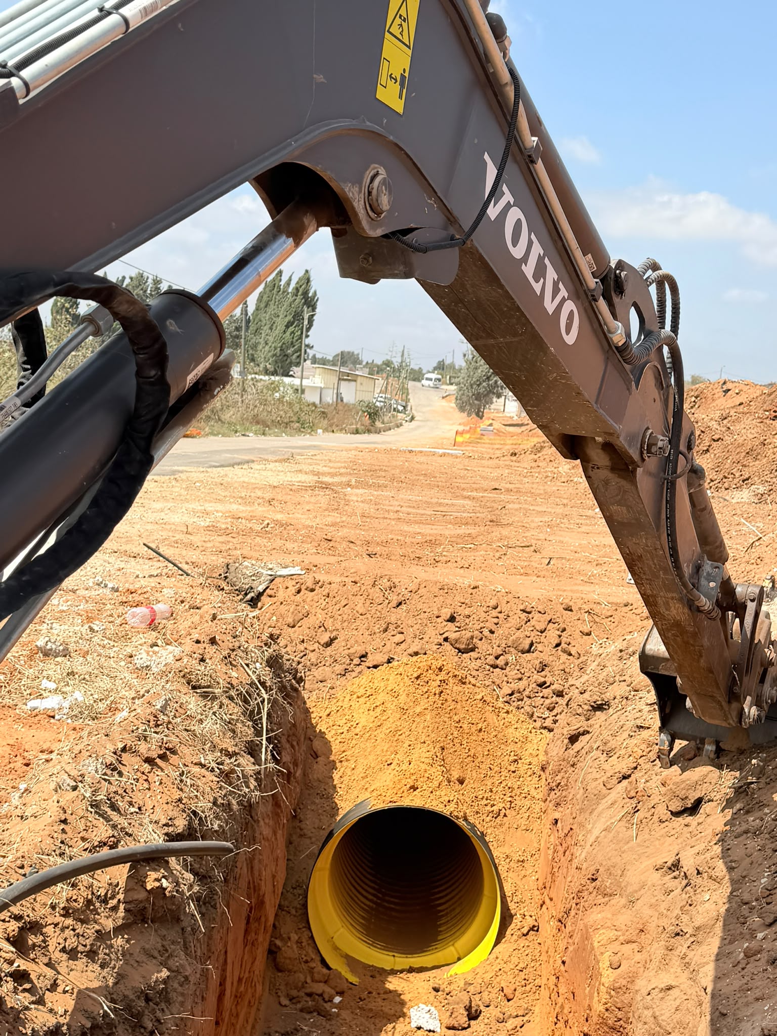 באגר מניח צינור שרשורי צהוב גדול בתעלה חפורה